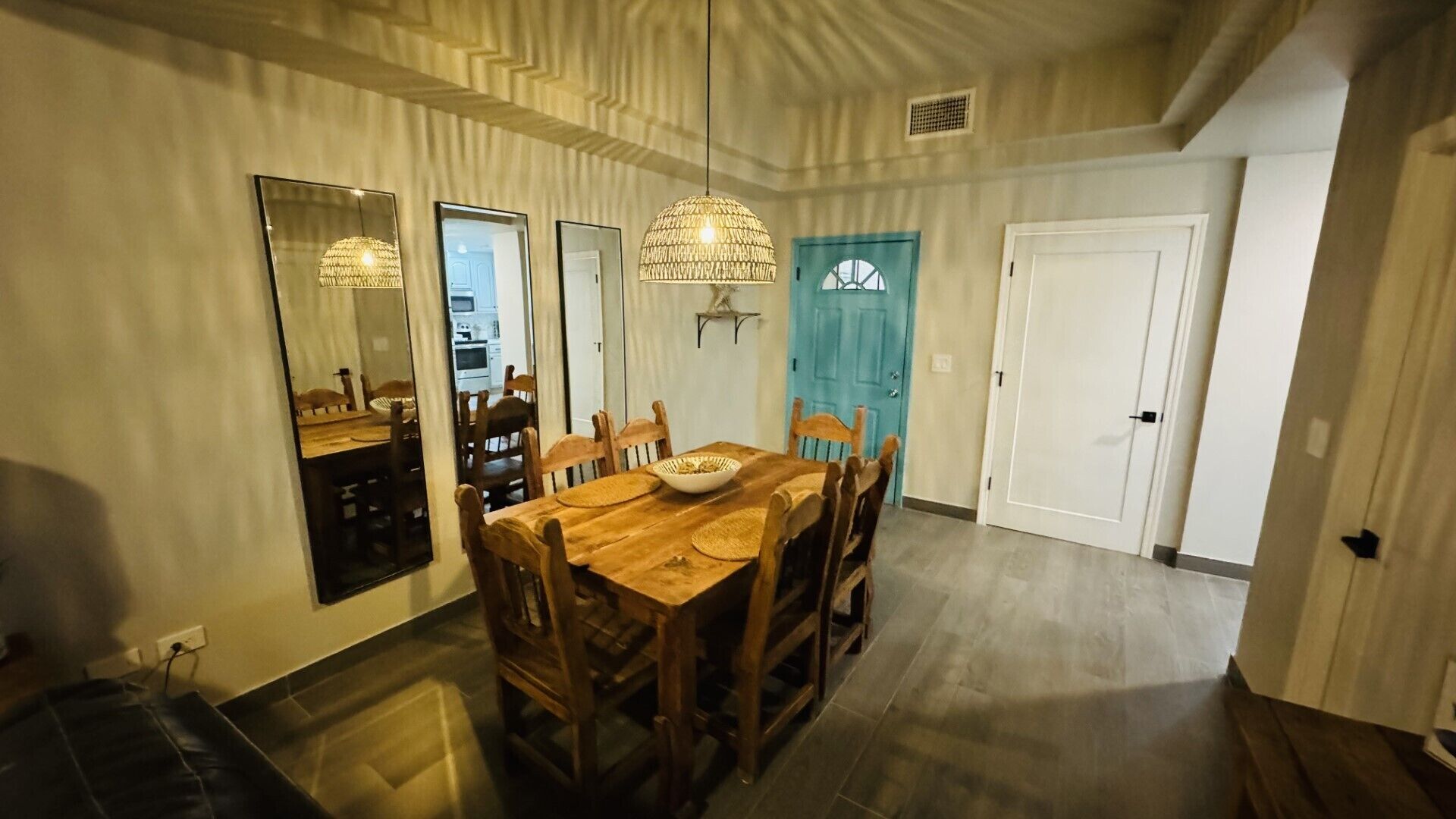 Comedor con una mesa y sillas de madera, una araña y una puerta azul al fondo.