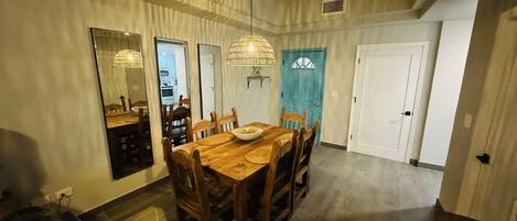 Comedor con una mesa y sillas de madera, una araña y una puerta azul al fondo.