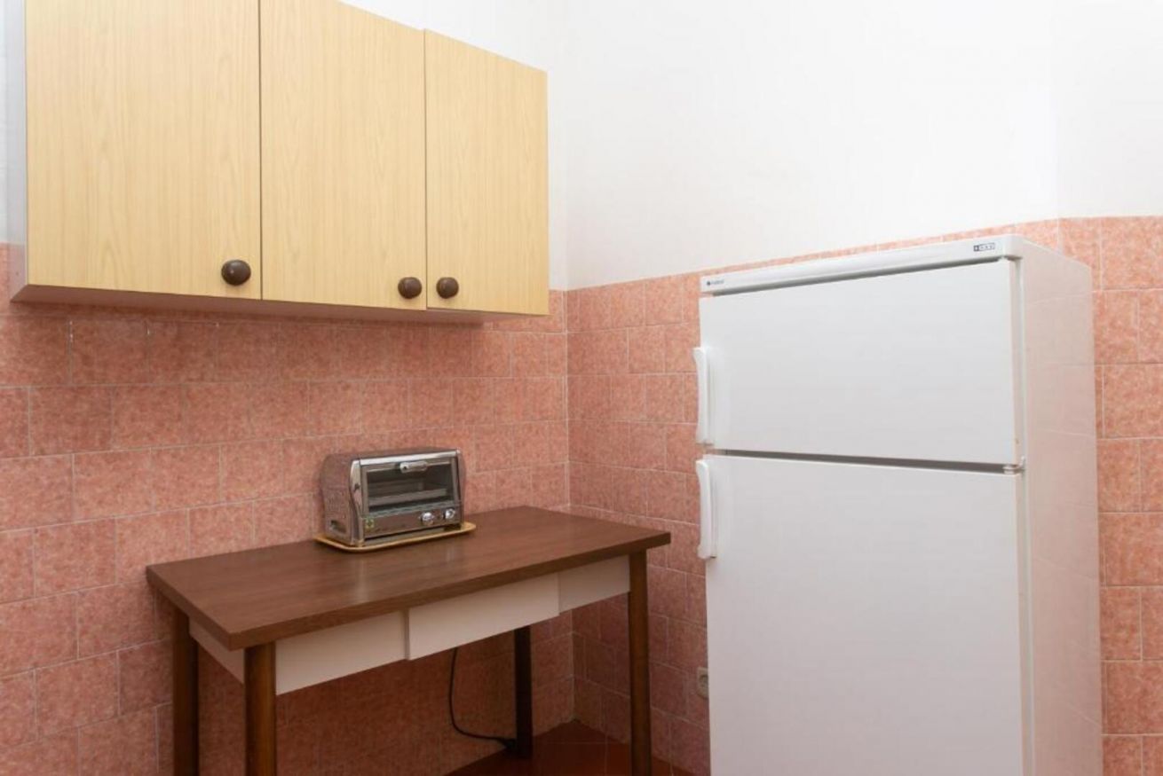 A small kitchenette with a wooden cabinet, a white refrigerator, and a toaster on a wooden table.