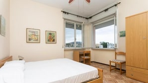 Un dormitorio con una cama, dos sillas, un armario de madera y dos cuadros en la pared.
