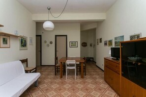 A room with a sofa, dining table, chairs, a TV, and a cabinet.