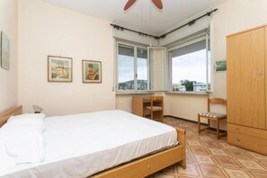 Un dormitorio con una cama, dos sillas, un armario de madera y dos cuadros en la pared.
