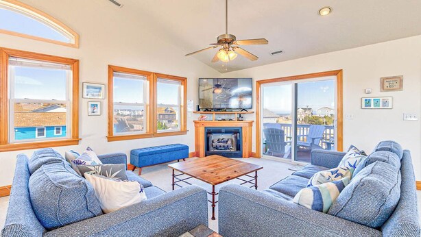 A spacious living room with a fireplace, large windows, and a ceiling fan.