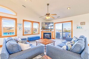 A spacious living room with a fireplace, large windows, and a ceiling fan.