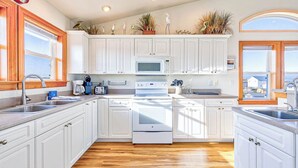 A kitchen with white cabinets, a microwave, a stove, and a sink. There are decorative items on the cabinets and a window with a view.