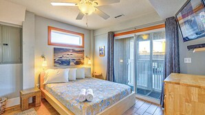 A bedroom with a bed, a ceiling fan, a TV, and a balcony with curtains.
