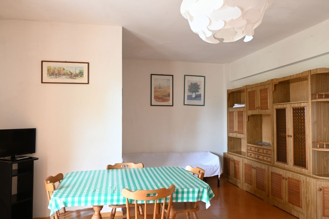 A dining area with a checkered table, chairs, a television on a stand, and wooden cabinets.