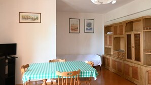 Un coin repas avec une table à carreaux, des chaises, un téléviseur posé sur un meuble et des armoires en bois.