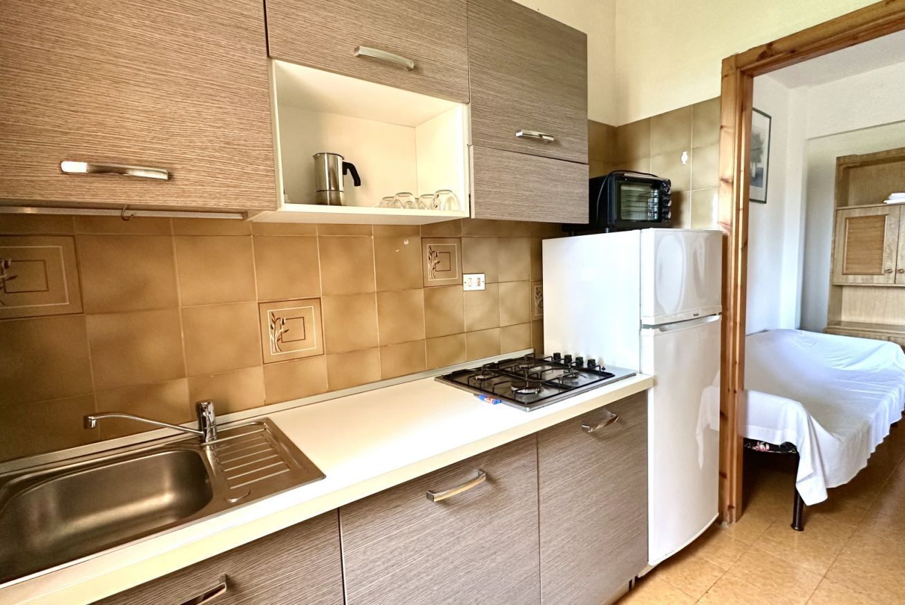 A compact kitchen with a sink, stove, and refrigerator, adjacent to a bedroom with a bed.