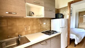 Une cuisine compacte équipée d’un évier, d’une cuisinière et d’un réfrigérateur, jouxtant une chambre à coucher avec un lit.