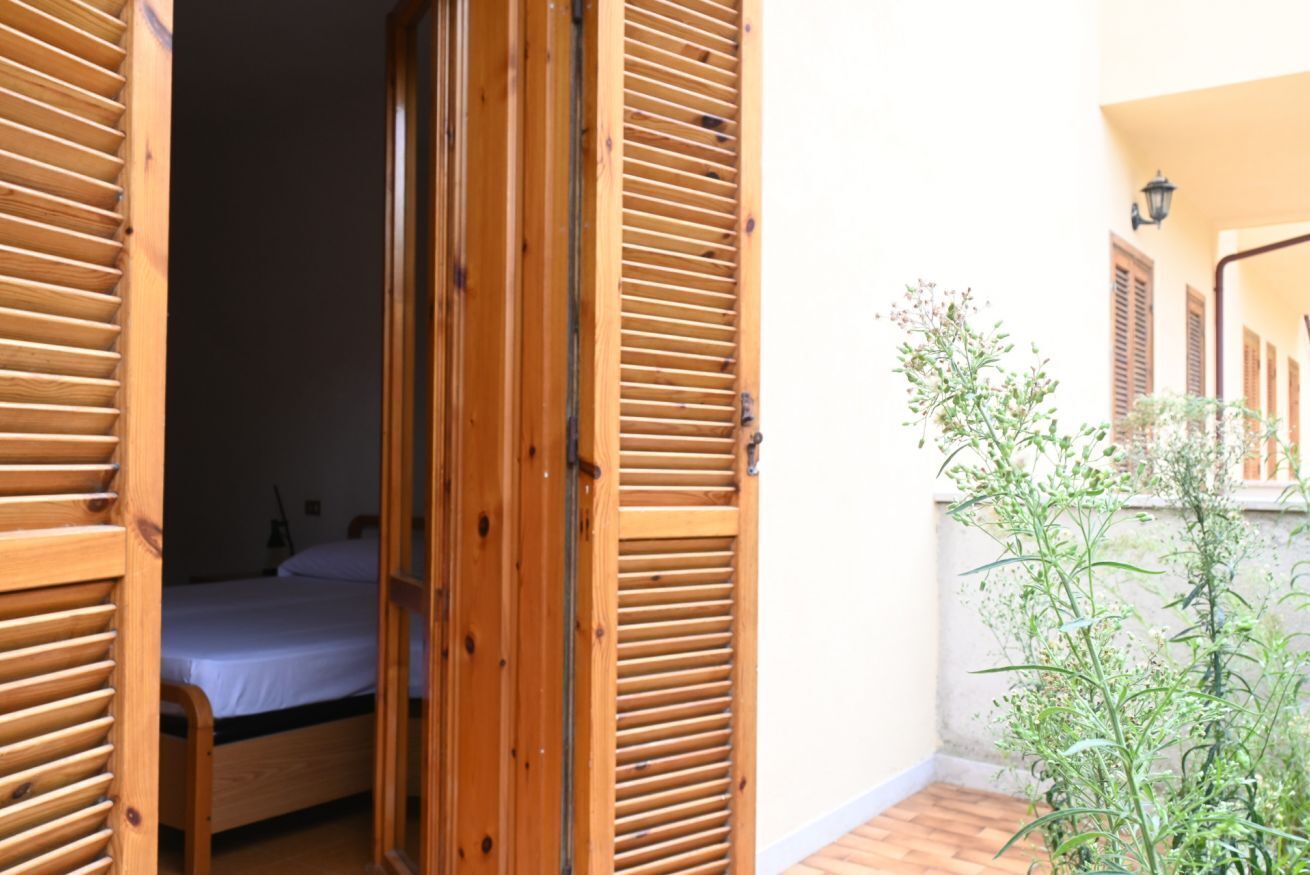 A room with a bed, wooden shutters, and a small balcony with plants.