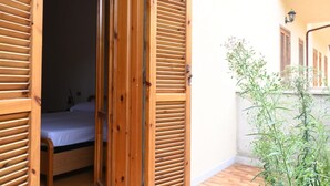 Une chambre avec un lit, des volets en bois et un petit balcon agrémenté de plantes.