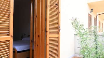 A room with a bed, wooden shutters, and a small balcony with plants.