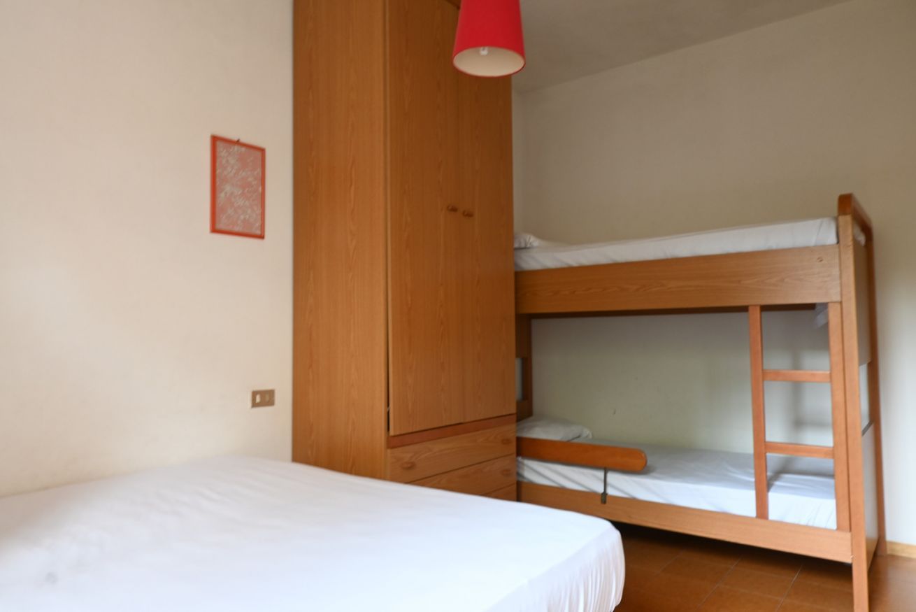 A bunk bed room with a wooden wardrobe and a red hanging light fixture.