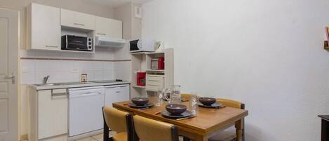 A compact kitchen with white cabinets, a microwave, a toaster, and a sink. There is a dining table with four chairs and a few dishes on it.