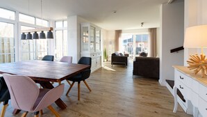 A spacious living area with a wooden dining table, chairs, a sofa, and a lamp. - NEW: Child-friendly holiday home, bicycles & handcart, 300m to the beach (Langeoog)