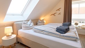A bedroom with a skylight, a bed with striped bedding, a bedside lamp, and a view of the city through a window. - NEW: Child-friendly holiday home, bicycles & handcart, 300m to the beach (Langeoog)