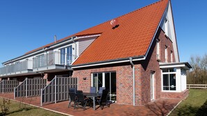 A modern two-story house with a red-tiled roof, a balcony, and a patio with outdoor furniture. - NEW: Child-friendly holiday home, bicycles & handcart, 300m to the beach (Langeoog)