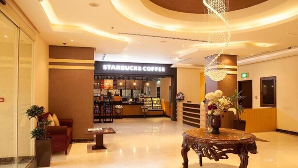 A Starbucks Coffee in a modern lobby with a reception desk, a seating area, and a decorative chandelier. - The Venue Resident (Mahboula)
