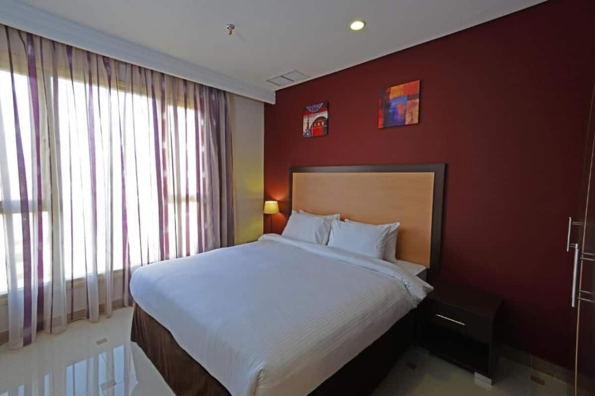 A hotel room with a large bed, a nightstand, a lamp, and two paintings on the wall.