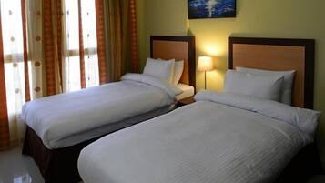Two single beds with wooden headboards and white bedding, a large window with sheer curtains, and a sailboat painting adorn this well-maintained room.