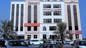 A tall building with multiple floors, featuring a mix of commercial spaces on the ground level including a KFC and a bank. - The Venue Resident (Mahboula)