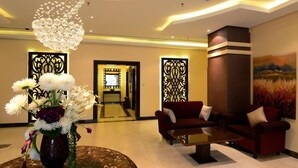 A lobby with a round table, red sofas, a chandelier, and decorative panels. - The Venue Resident (Mahboula)