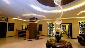 A lobby with a reception desk, a potted plant, a decorative chandelier, and a seating area. - The Venue Resident (Mahboula)
