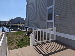 A deck with a white railing, a grassy area, and a body of water with docks in the background. - Canal-front, walk to the beach/boardwalk (Ocean City)