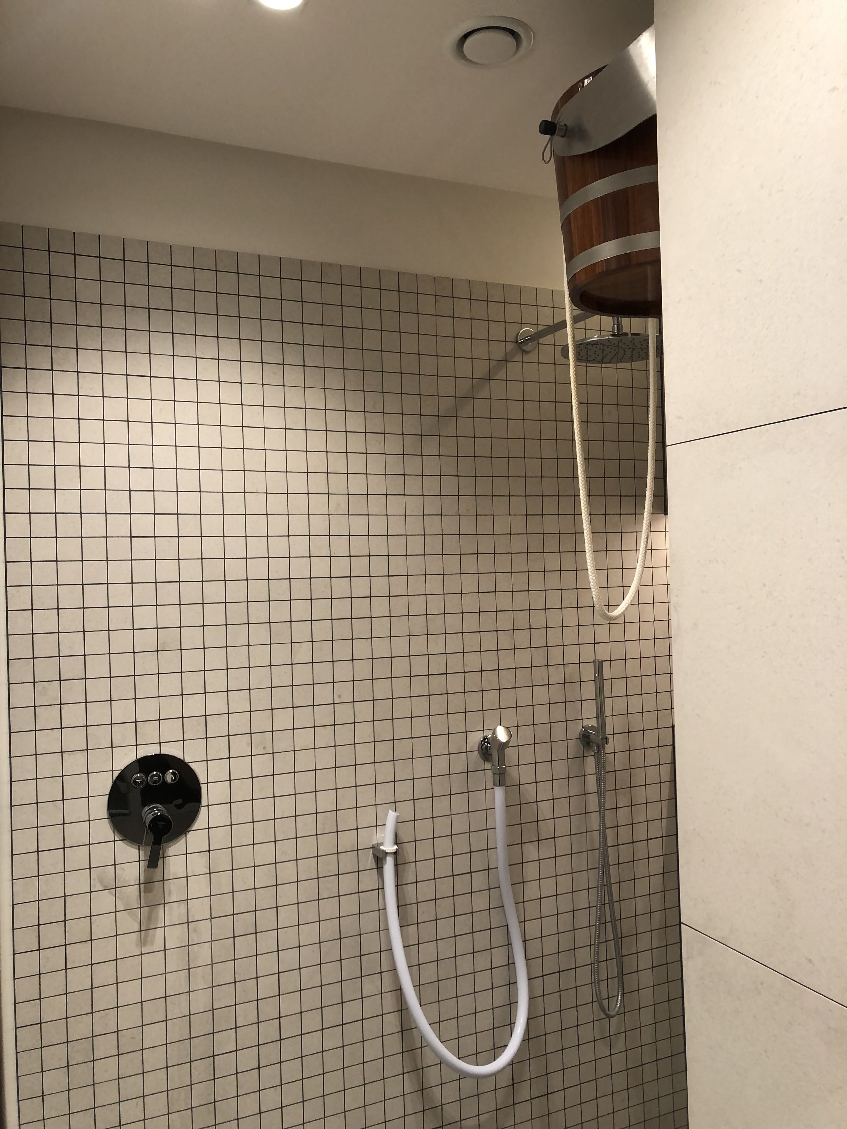 A shower area with a tiled wall, a handheld showerhead, and a wall-mounted faucet.