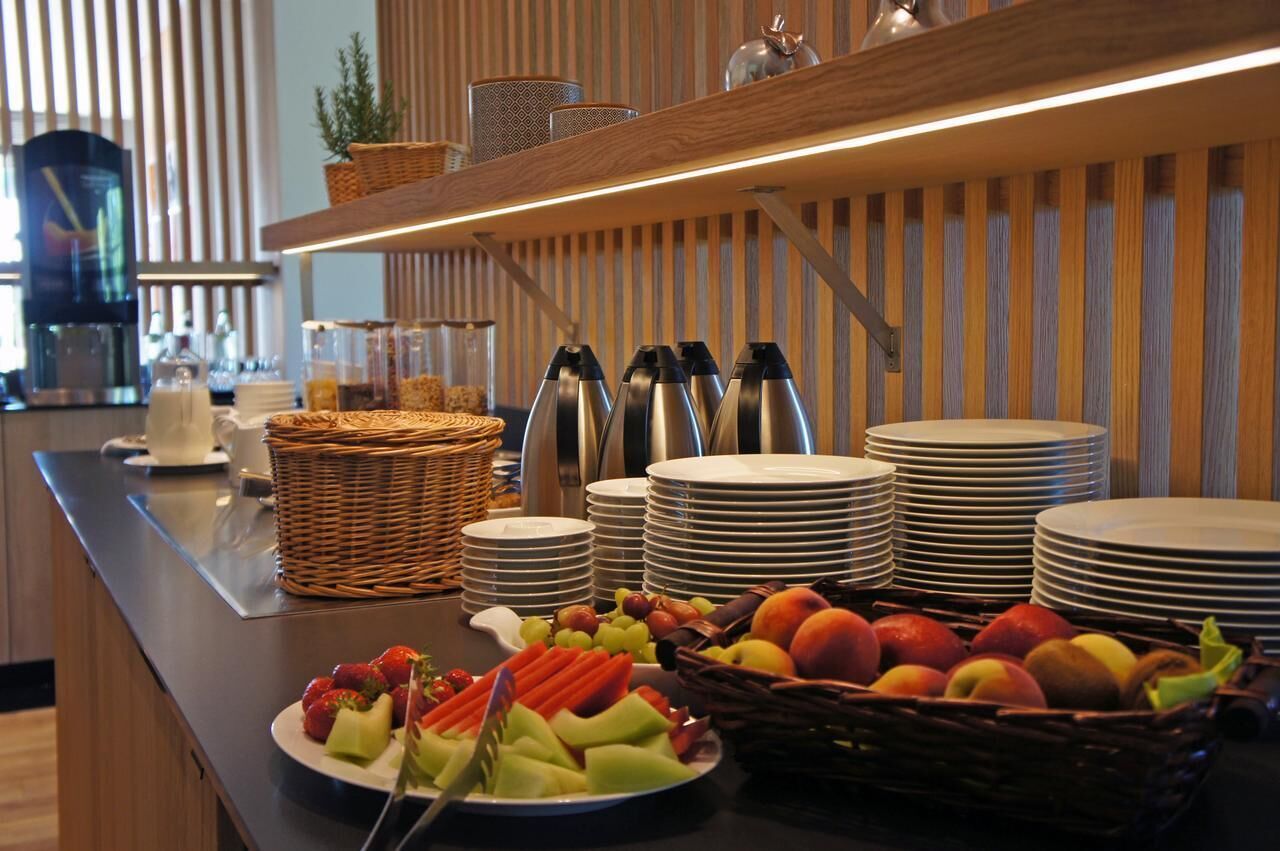 A buffet setup with plates, bowls, and a variety of fruits and vegetables.