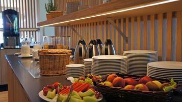 A buffet setup with plates, bowls, and a variety of fruits and vegetables.