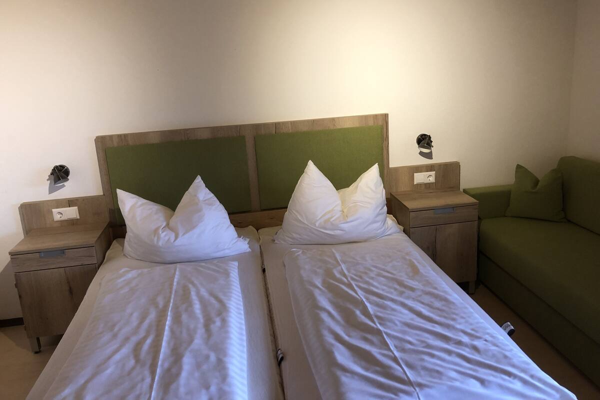 Une chambre double avec deux lits simples, des têtes de lit en bois, des tables de chevet et un canapé vert.