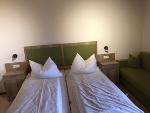 Habitación doble con dos camas individuales, cabeceros de madera, mesitas de noche y un sofá verde.