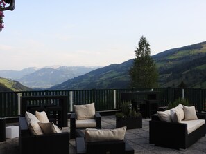 An outdoor seating area with wicker furniture and cushions, overlooking a mountainous landscape. - Ertlschweigerhaus (Irdning-Donnersbachtal)