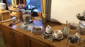 Een ontbijtbuffet met diverse etenswaren, waaronder kommen met ontbijtgranen, een koffiehoek en een hartvormige decoratie aan de muur.