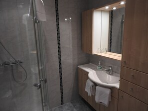 Un baño moderno con ducha de vidrio, lavamanos blanco y armarios de madera.