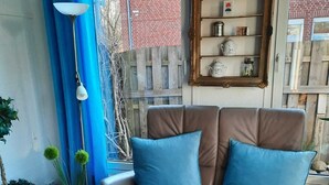 A cozy living room with a brown leather sofa, blue cushions, a blue vase with green flowers, and a wooden coffee table with a blue coaster and glasses. - Vacation luck hit (Meppen)