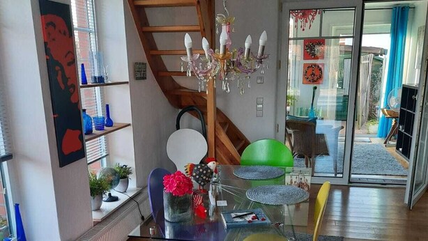 A modern living room with a glass dining table, red and yellow chairs, a wooden staircase, and a view of the outside. - Vacation luck hit (Meppen)