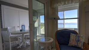 A room with a view of the water, a dining area with white chairs, a blue sofa, and a small table with a lamp. - First Floor, 2 BD, 2 BA Condo, Bayside Views, Pool, Tennis, and Many Free Activities! (Ocean View)
