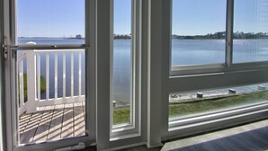 A room with a large window overlooking a calm body of water, a wooden deck, and a white railing. - First Floor, 2 BD, 2 BA Condo, Bayside Views, Pool, Tennis, and Many Free Activities! (Ocean View)