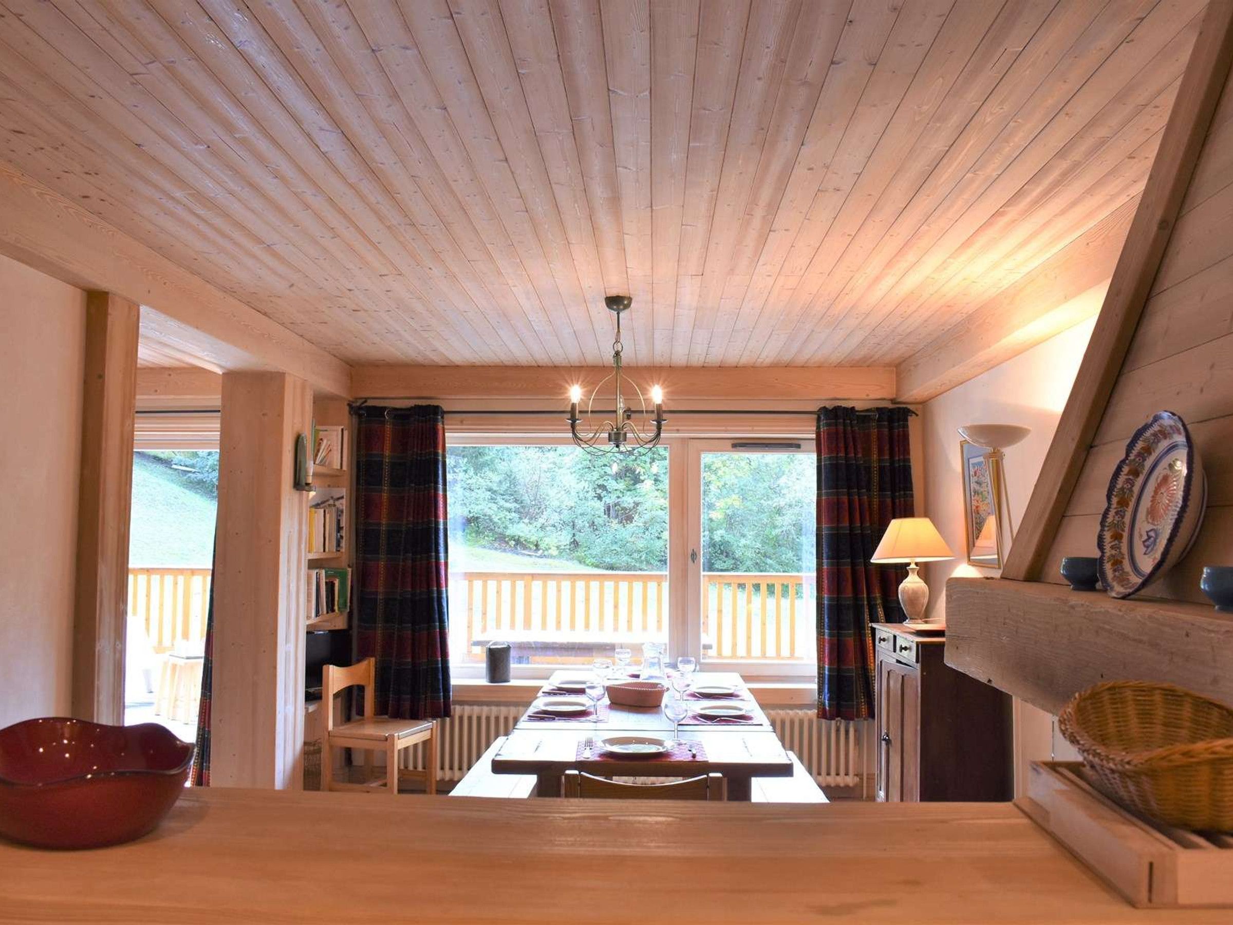 A dining area with a wooden table, chairs, a chandelier, and a view of the outdoors.