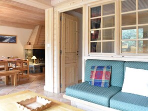 Ein gemütliches Zimmer mit Holzbalkendecke, einer Couch mit gemusterten Kissen, einem Esstisch mit Stühlen und einem Fenster mit Vorhängen.