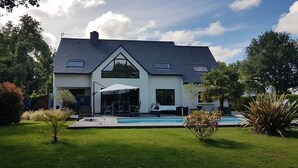 A modern house with a swimming pool, a covered patio, and a well-maintained lawn.