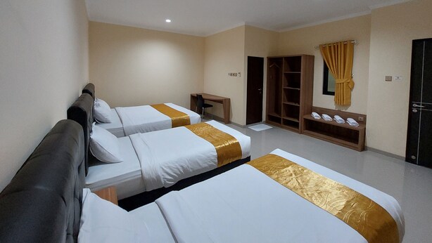 Ein Hotelzimmer mit drei Betten, einem Schreibtisch, einem Kleiderschrank und einem Badezimmer.