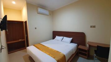 A hotel room with a bed, a desk, an air conditioning unit, and a wardrobe.