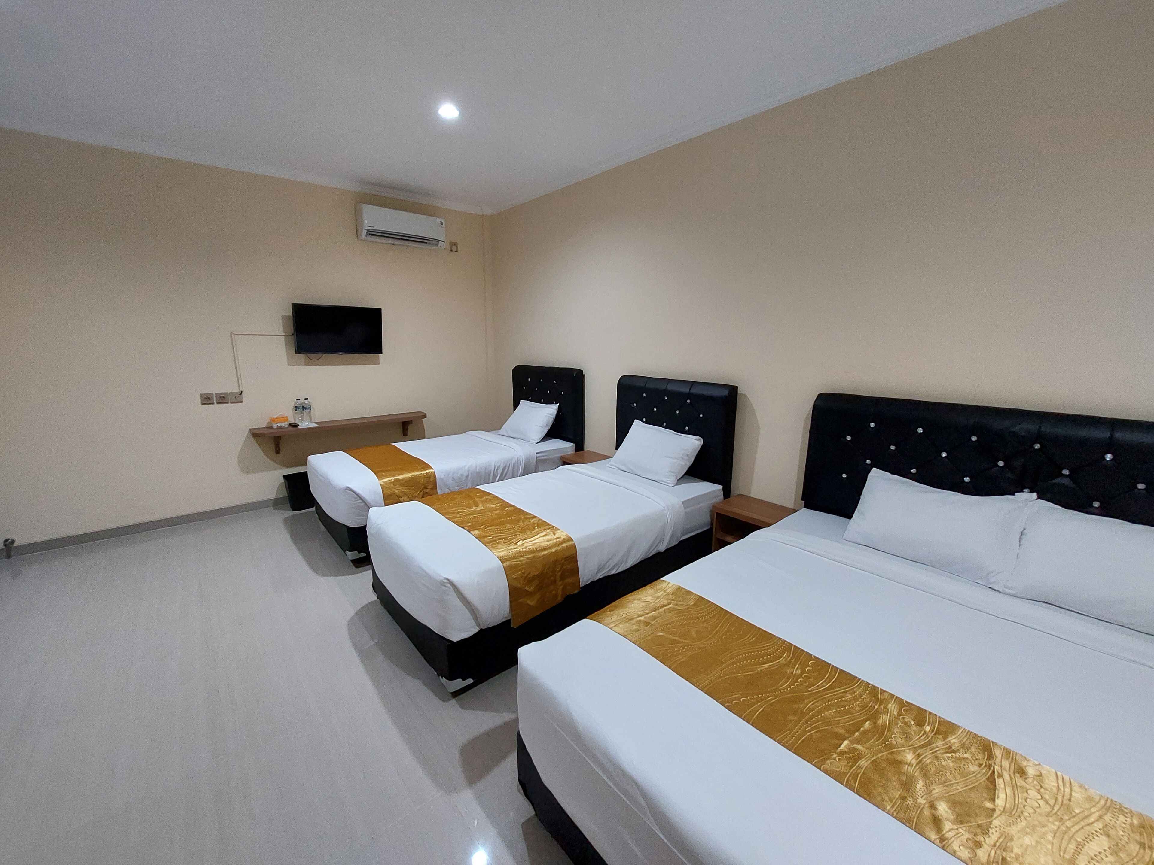 A hotel room with three beds, a flat-screen TV mounted on the wall, and a small table with a bottle of water.