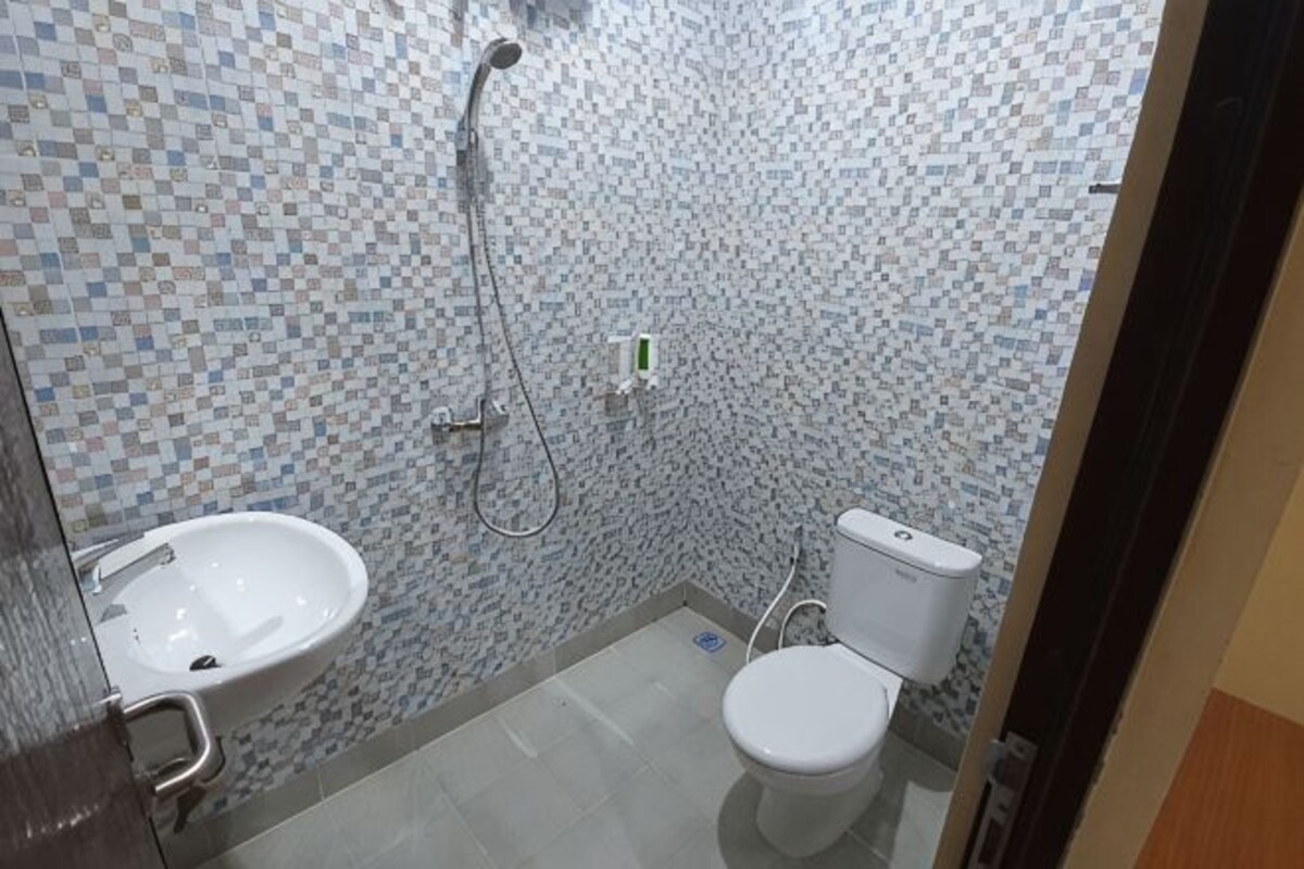A small bathroom with a tiled wall, a sink, a toilet, and a shower.