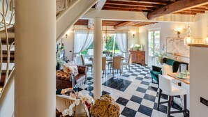 Una habitación amplia con piso a cuadros, un área de comedor con mesa y sillas, y una escalera con barandilla decorativa.