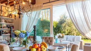 Un comedor con una mesa dispuesta para cuatro personas, una araña y vistas del jardín a través de amplios ventanales.